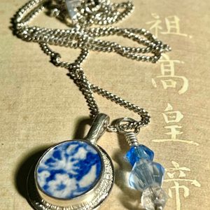 Deux pendentifs en argent sur une chaîne avec en serti un morceau de faïence à décor bleu et blanc et trois perles de cristal de Bohème.