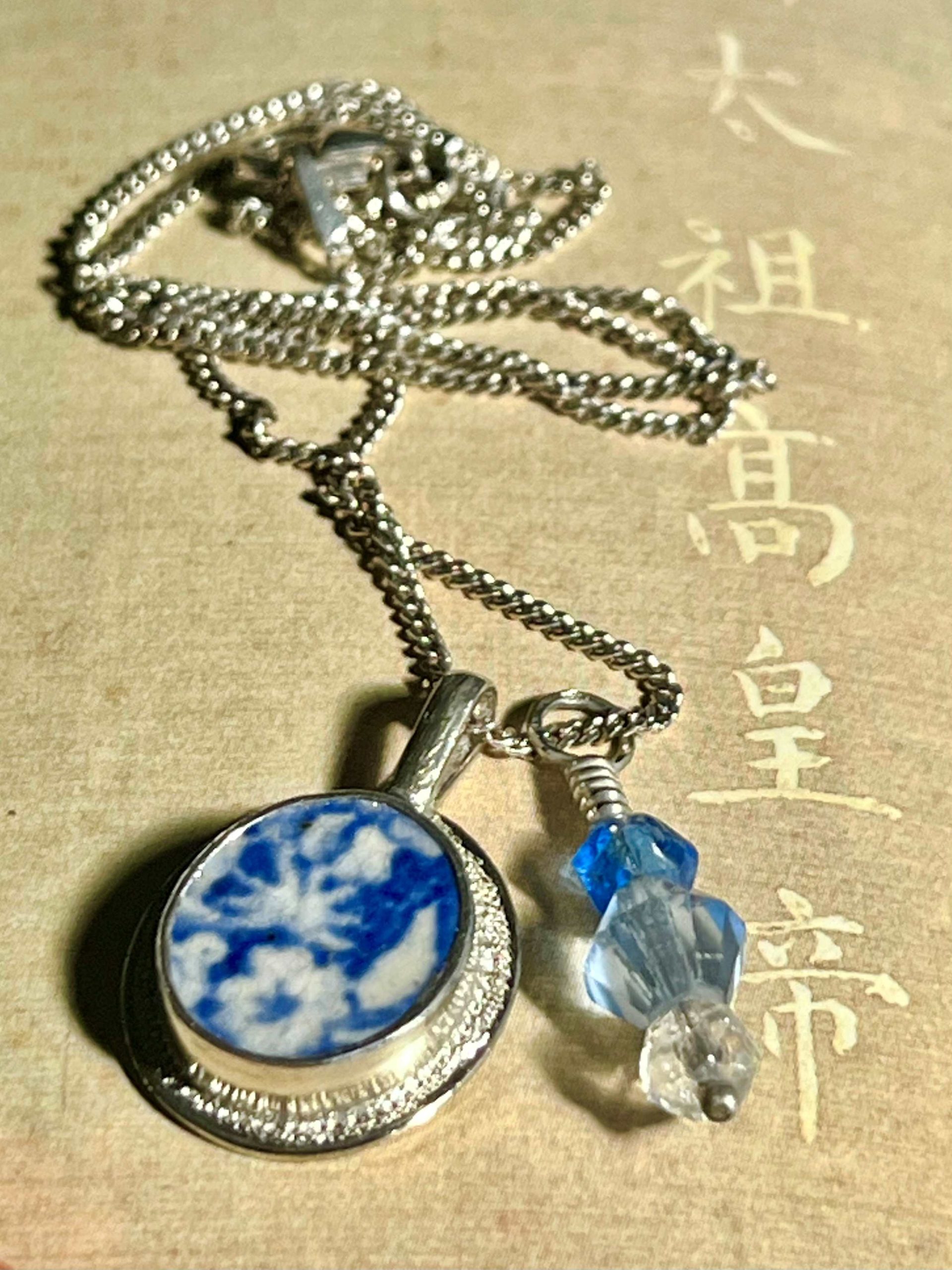 Deux pendentifs en argent sur une chaîne avec en serti un morceau de faïence à décor bleu et blanc et trois perles de cristal de Bohème. 