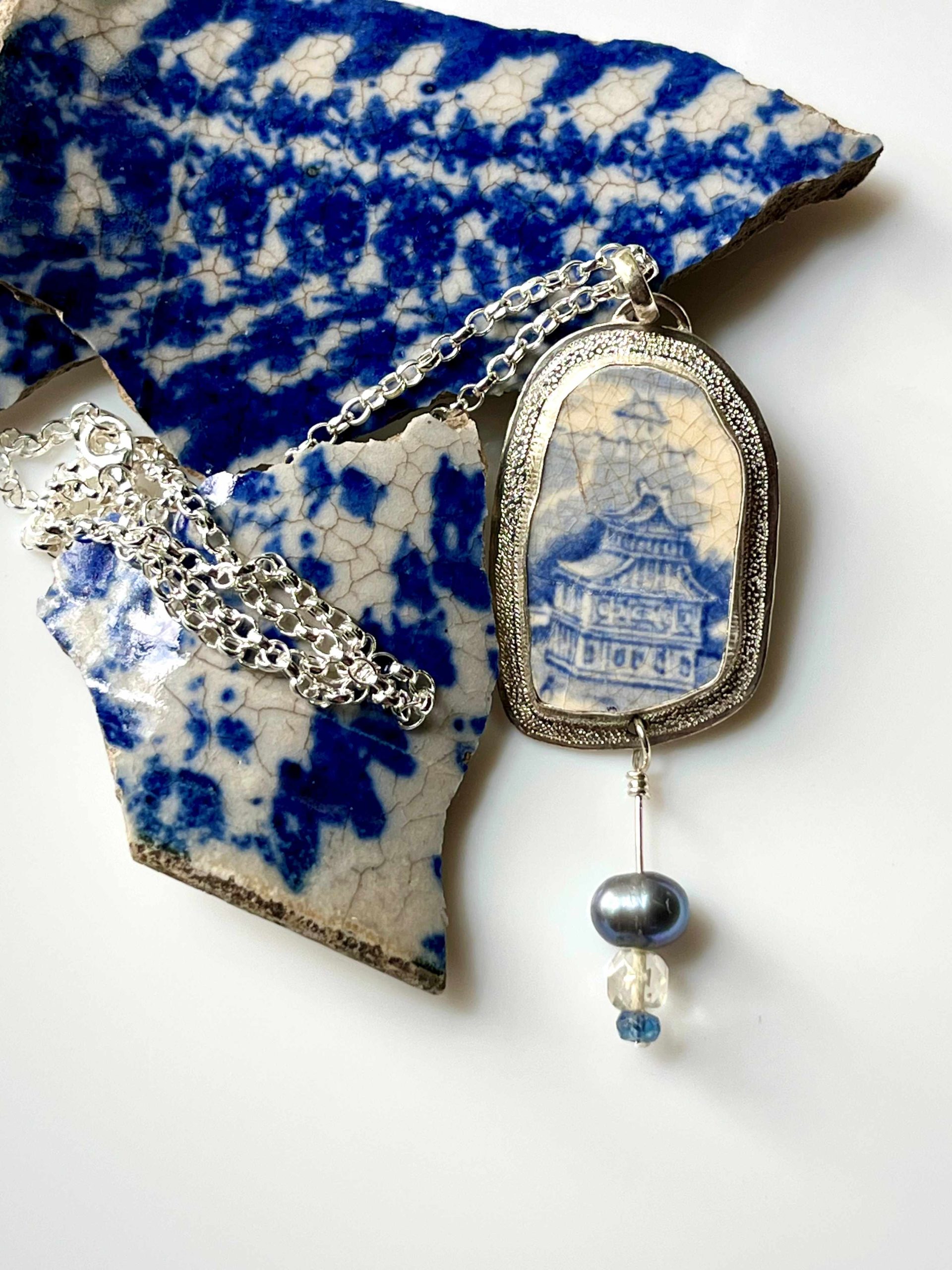 Pendentif en argent avec en serti un morceau de faïence à décor bleu et blanc et trois perles.