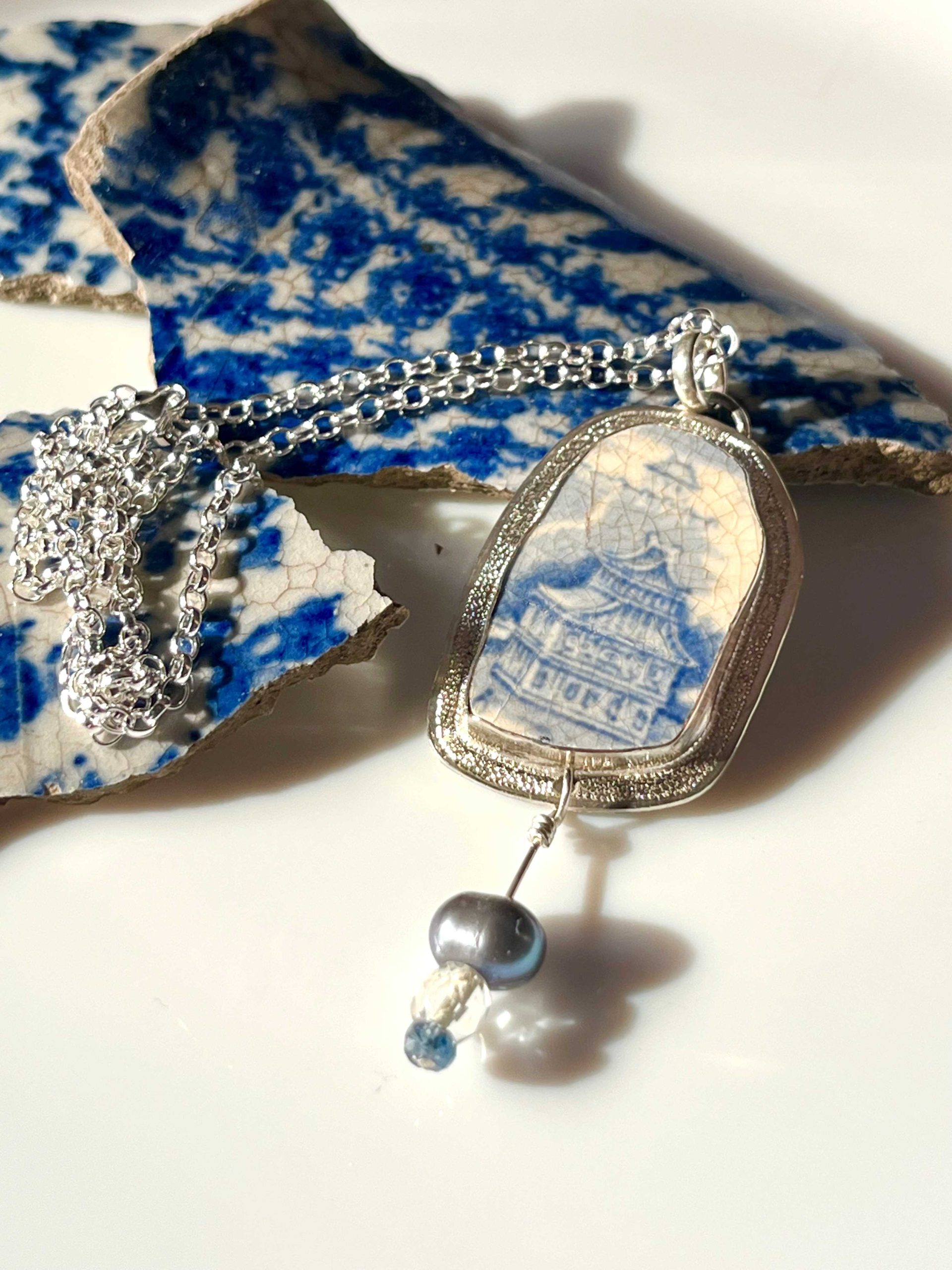 Pendentif en argent avec en serti un morceau de faïence à décor bleu et blanc et trois perles.